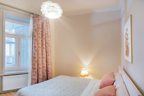 Ein Schlafzimmer mit einem Bett, einem Fenster, einer Heizung, einer Lampe und einem an der Wand hängenden Bild.