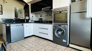 Una cocina moderna con lavavajillas, horno y lavadora, armarios blancos y piso de baldosas.