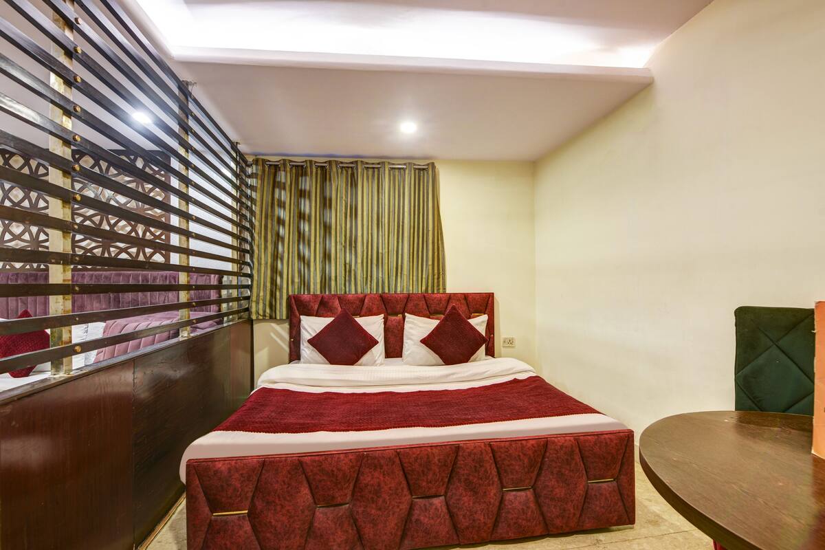 A bedroom with a bed, a wooden headboard, a red bedspread, a green upholstered chair, and a wooden table.