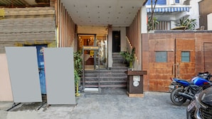 A building entrance with a staircase leading to a door, a parked motorcycle, and a closed shutter on the left. - Hotel WK Comfort Inn (New Delhi)