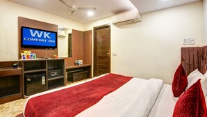 A hotel room with a bed, a television displaying 'WK Comfort Inn,' a ceiling fan, an air conditioning unit, and a wooden wardrobe. - Hotel WK Comfort Inn (New Delhi)