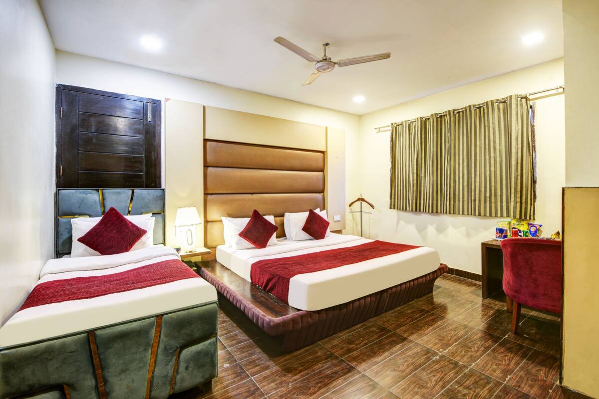 A hotel room with two beds, a ceiling fan, a window with curtains, and a small table with snacks.