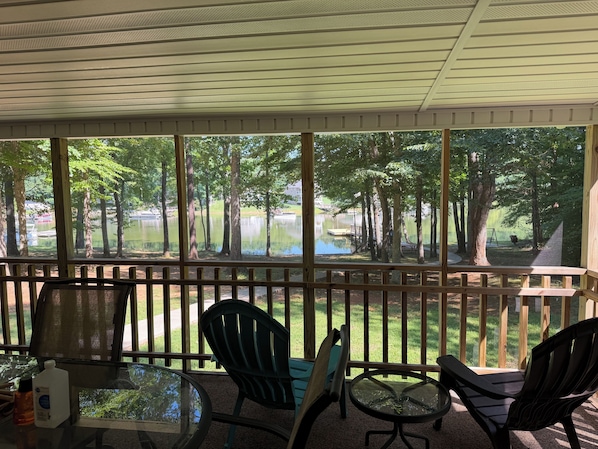 A covered outdoor area with a table and chairs, a view of a lake and trees, and a wooden fence. - Skipper's Cove, Lakefront Family Escape w/ Private Dock, Kayaks, Fire Pit & more (Lexington)
