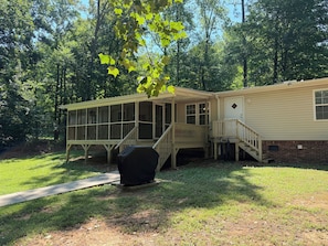 A two-story mobile home with a covered porch and a small deck, surrounded by a grassy yard and trees. - Skipper's Cove, Lakefront Family Escape w/ Private Dock, Kayaks, Fire Pit & more (Lexington)