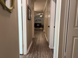 Ein Flur mit Holzdielen, weißen Wänden und einem Deckenventilator.