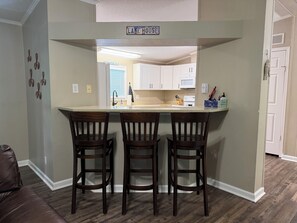 Una cocina con barra, tres taburetes de madera y un cartel sobre la barra que dice 'LAKE HOUSE'.