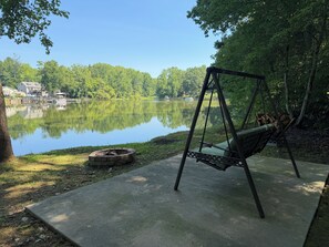 Un fauteuil suspendu près d’un lac, avec un foyer et une jetée en arrière-plan.