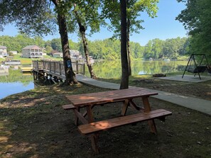 A picnic table with benches, a swing, and a wooden dock extending into a lake. - Skipper's Cove, Lakefront Family Escape w/ Private Dock, Kayaks, Fire Pit & more (Lexington)