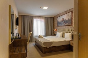 Quarto de hotel com cama, televisão, escrivaninha com cadeira, abajur e um quadro na parede.