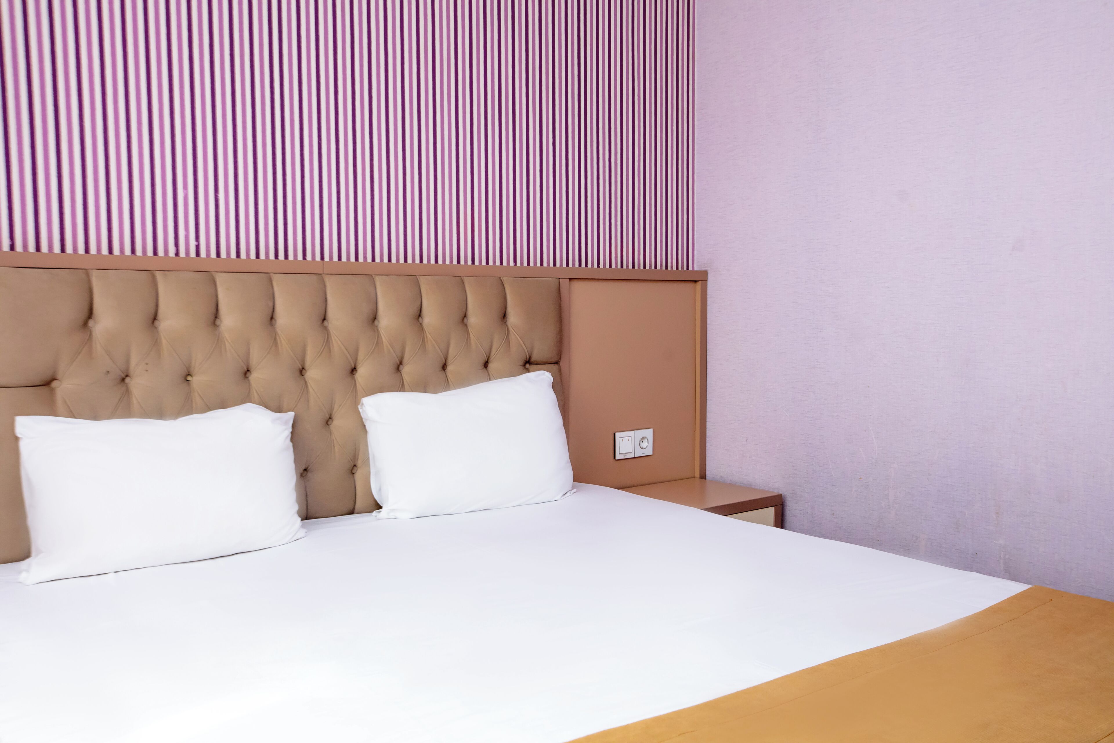 A neatly made bed with a tufted headboard, white pillows, and a wooden bedside table.