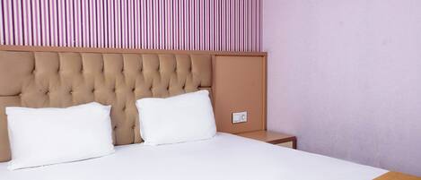 A neatly made bed with a tufted headboard, white pillows, and a wooden bedside table.