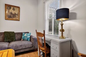 Ein Zimmer mit einer Couch, einem Holzstuhl, einer Lampe, einer Heizung und einem Fenster mit Jalousien.