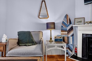 Ein Wohnzimmer mit einer Couch, einer Lampe, einem Kamin und einer Wand mit einem geometrischen Gemälde.