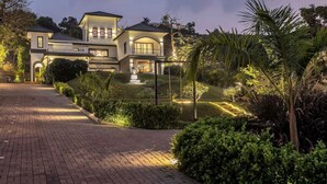 A large, two-story house with a well-maintained garden, a statue, and a paved driveway. - Lavender Villa by BasilStays (Calangute)