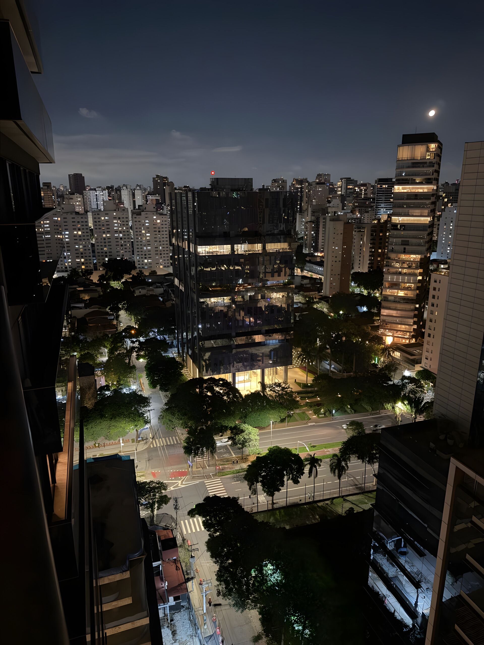 Une vue nocturne d’une ville, avec de hauts immeubles, un passage piéton et une rue où circulent des véhicules.