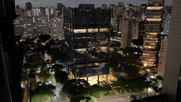 A nighttime cityscape with high-rise buildings, a crosswalk, and a street with vehicles. - Luxury studio apartment in Vila Olímpia - panoramic view and garage. (São Paulo)