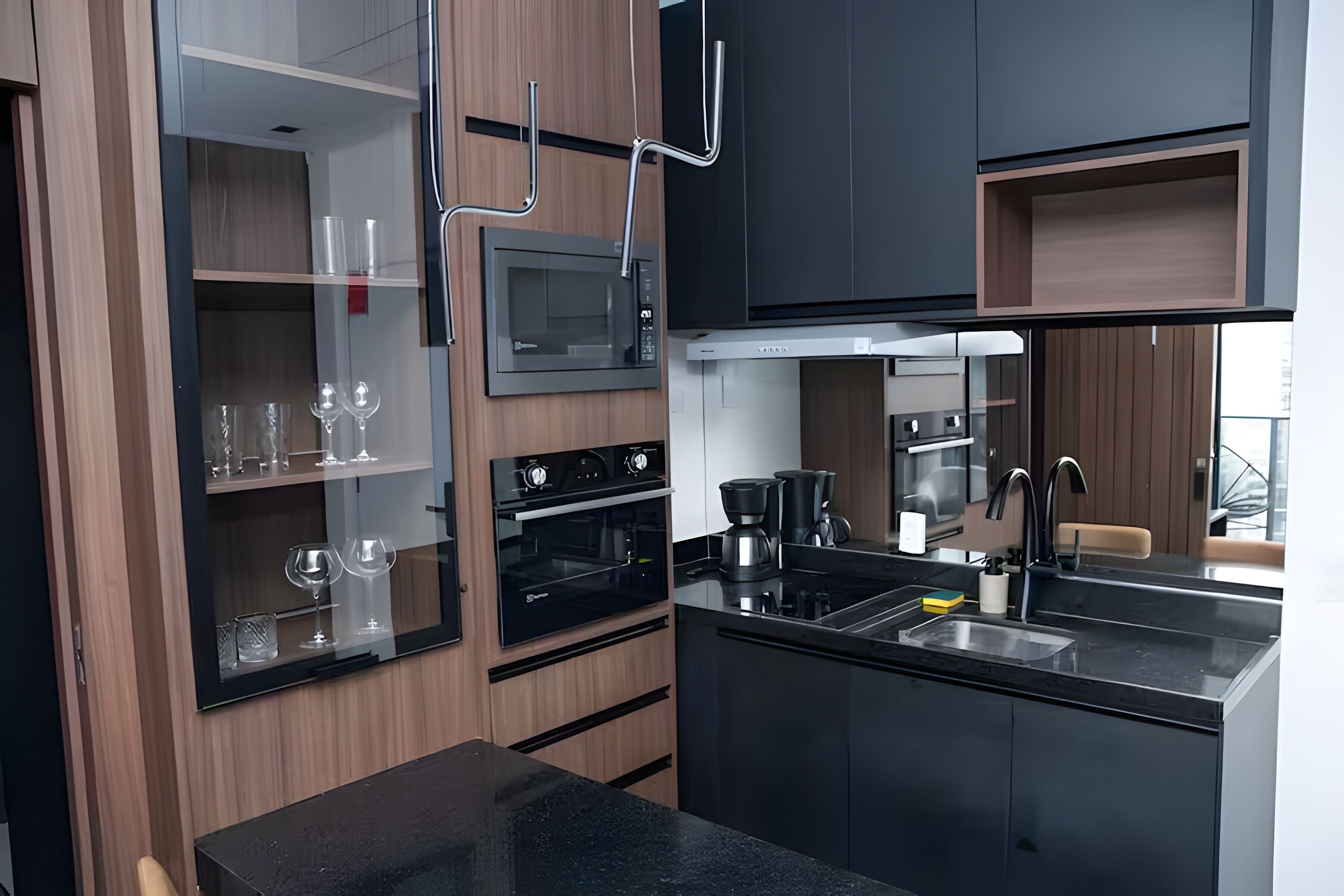 Une cuisine moderne dotée d’appareils électroménagers intégrés, d’un plan de travail noir et de meubles de rangement en bois.