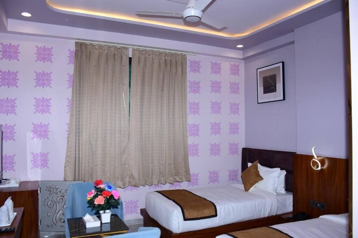 Habitación de hotel con cama, escritorio con un florero y ventilador de techo, además de papel tapiz estampado.