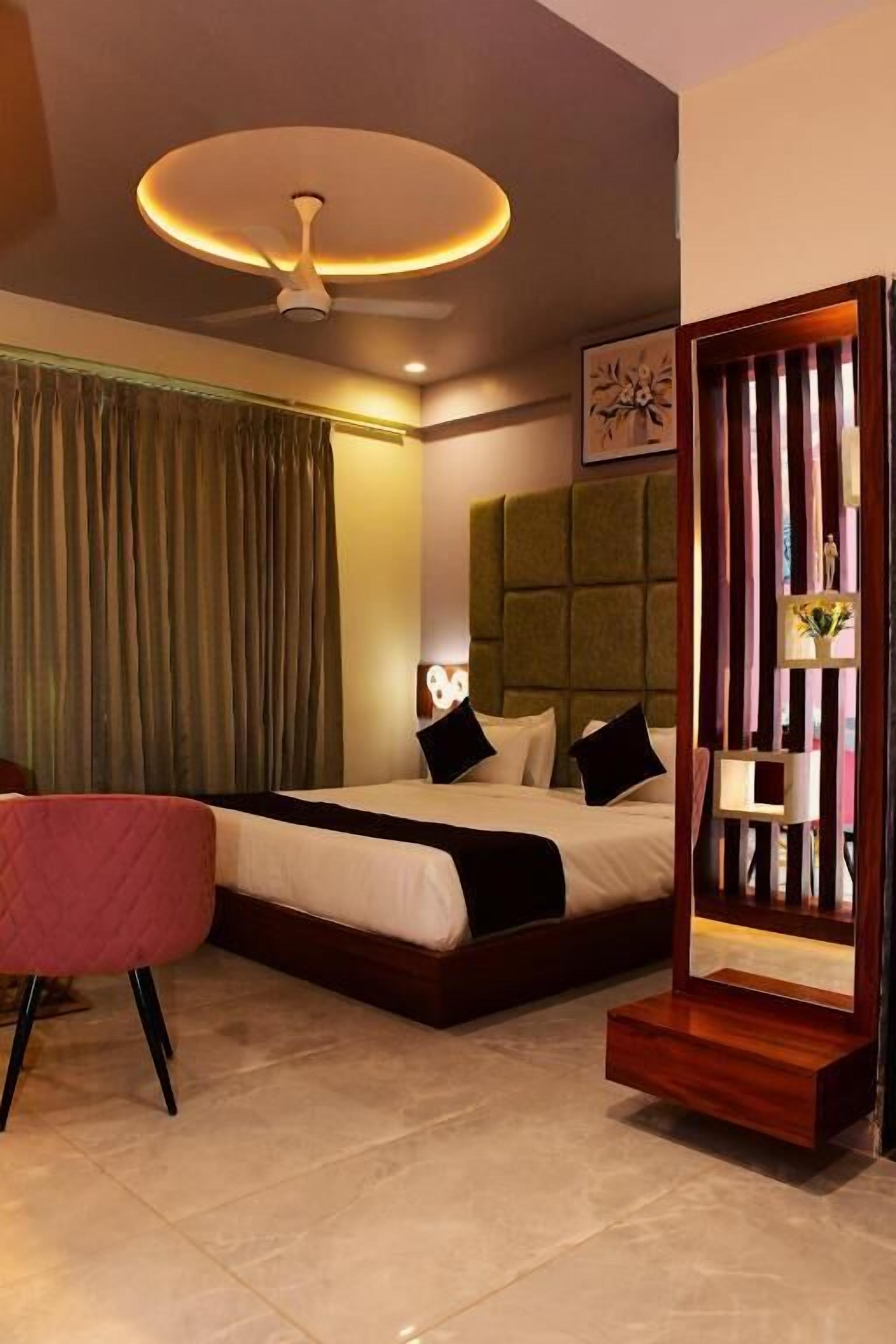 A hotel room with a bed, a chair, a bedside table, a mirror, and a ceiling fan.