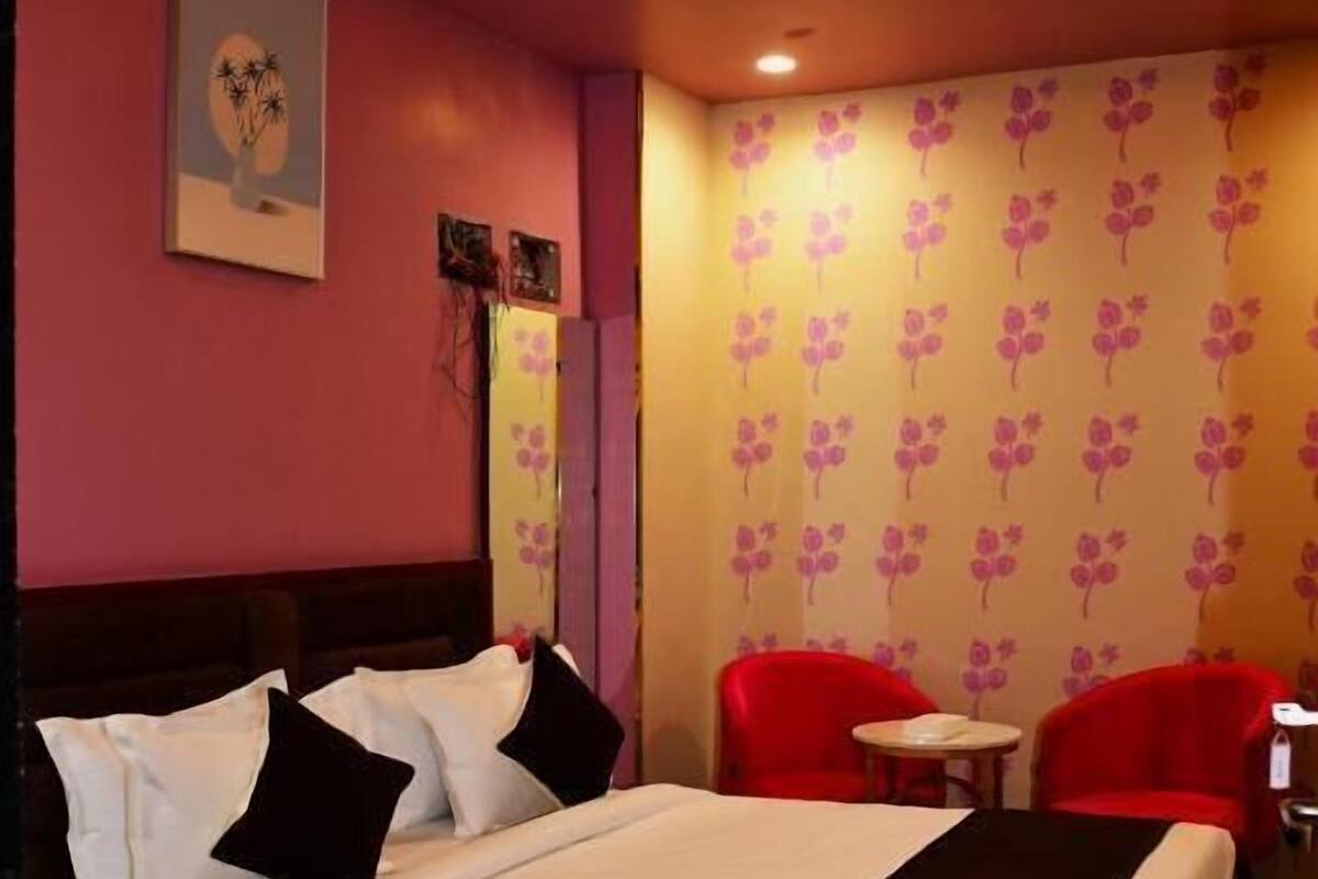 Habitación de hotel con una cama, dos sillas rojas, una mesita y una lámpara en el techo.