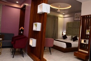 A modern hotel room with a bed, a seating area with chairs, a small table, a decorative wall panel, and a ceiling light fixture. - Foxoso Fiori Khatu Shyam (Danta Ramgarh)