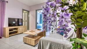 Uma sala de estar com televisão, móveis de madeira e uma planta com flores roxas.