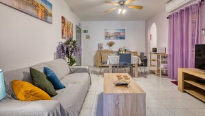 Uma sala de estar com sofá, mesa de centro, área de jantar com mesa e cadeiras, televisão e obras de arte nas paredes.