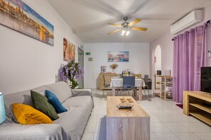 Een woonkamer met een bank, een salontafel, een eethoek met een tafel en stoelen, een televisie en kunstwerken aan de muren.