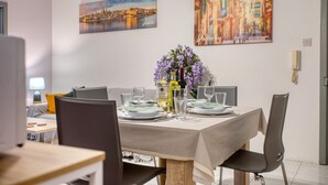 Uma sala de jantar com uma mesa posta para quatro pessoas, um vaso de flores roxas e duas pinturas nas paredes.