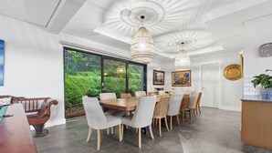 A dining area with a large table and chairs, a bench, and a view of greenery outside. - Coral House - Staynest Guesthouse (Ballito)