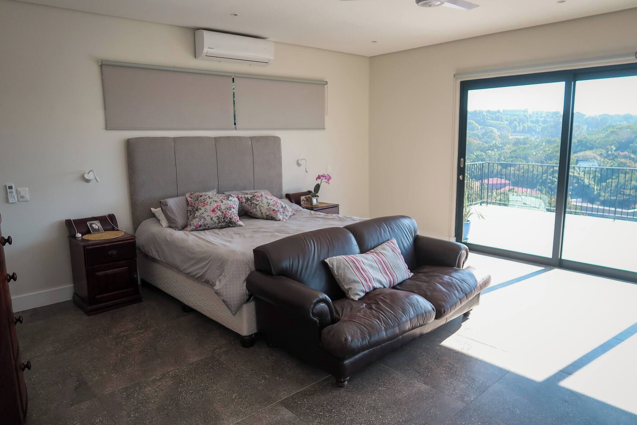 A bedroom with a bed, a leather sofa, a nightstand, and a large window with a view.