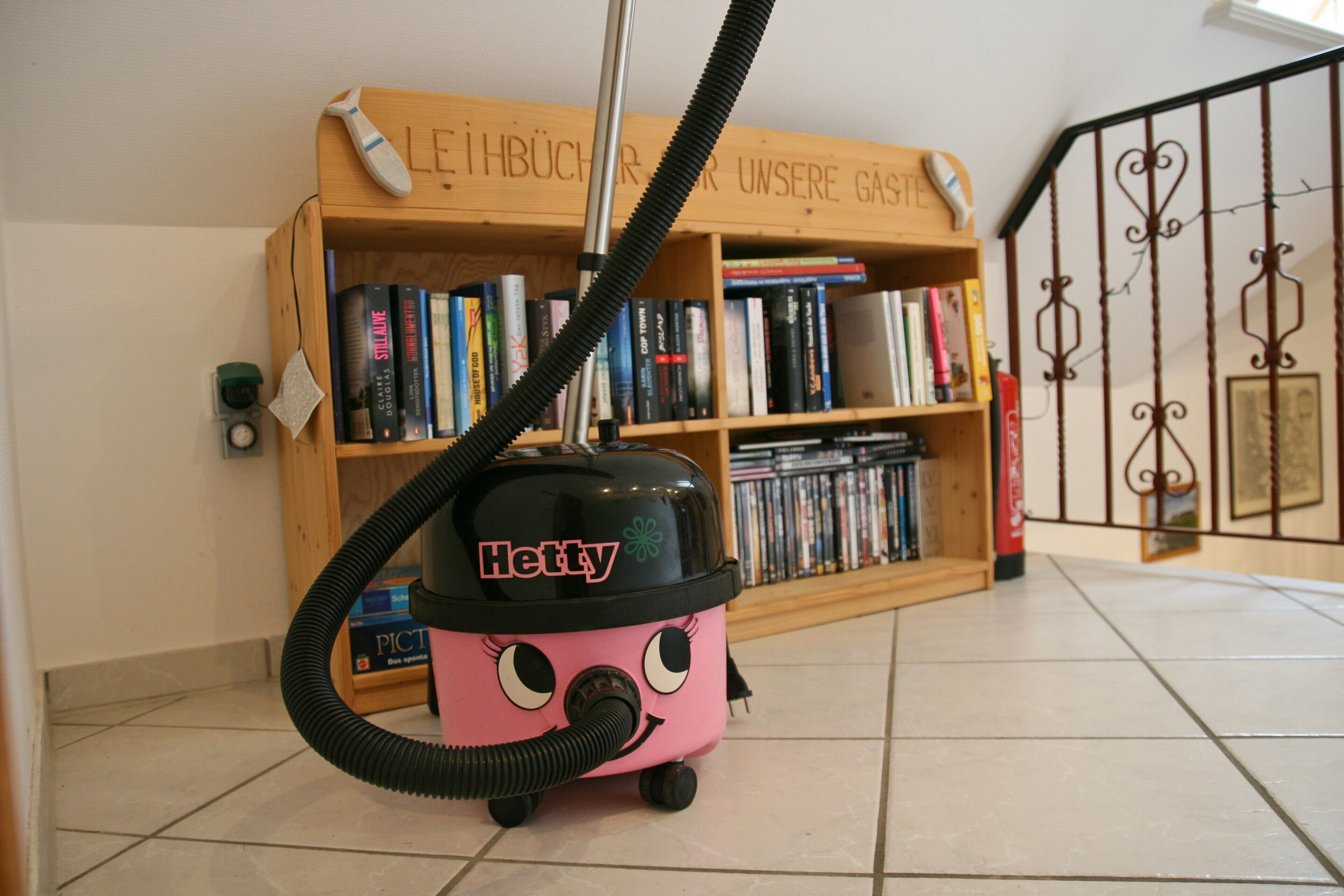 A vacuum cleaner in a room with a bookshelf and a decorative metal gate.