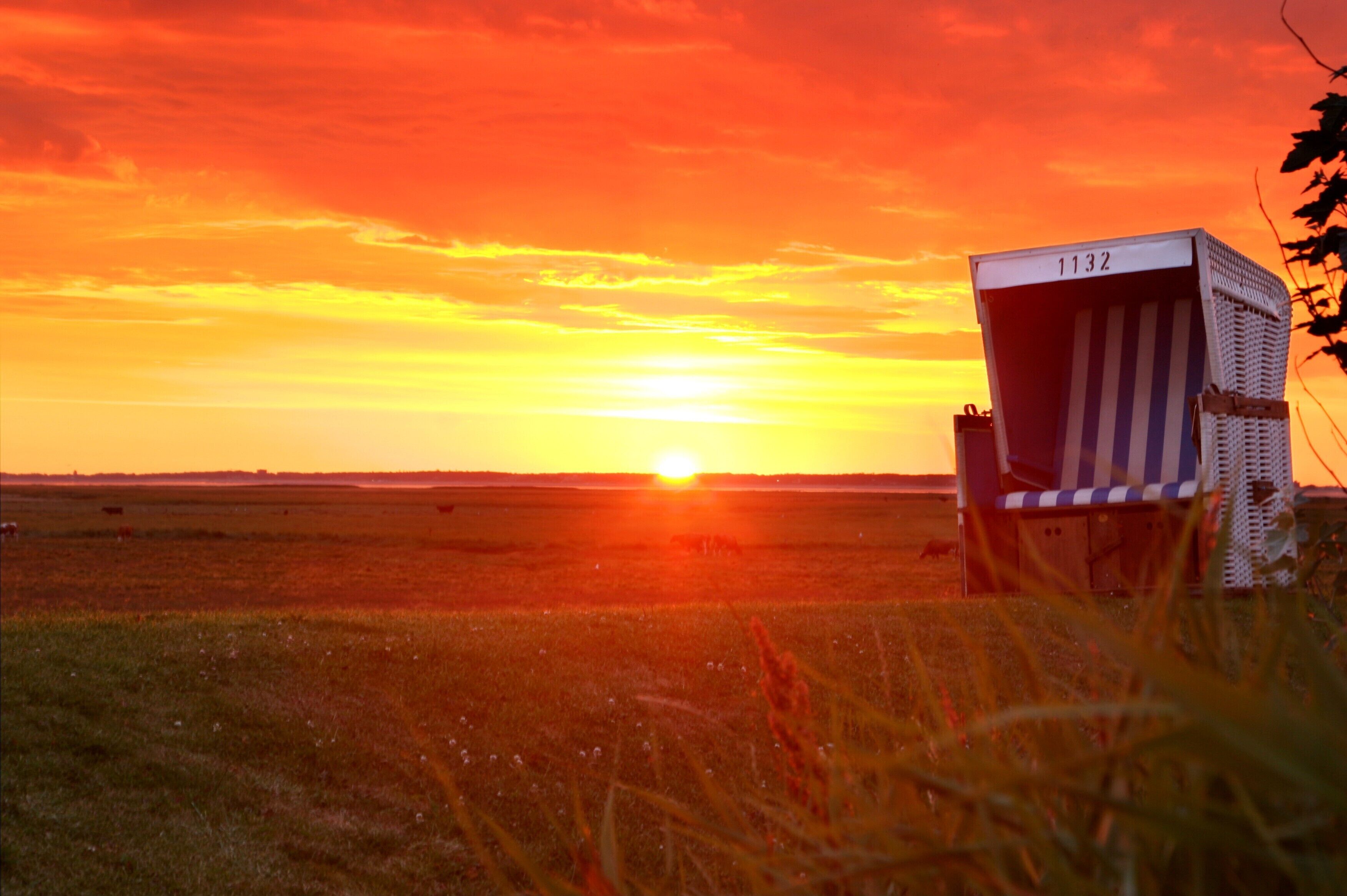 A beach chair with the number 1132, a sunset, and a field.