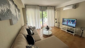 Ein Wohnzimmer mit einer Couch, einem Couchtisch, einem Fernseher und Blick ins Freie durch ein Fenster.