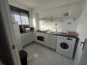A compact kitchen with a washing machine, a stove, a sink, and a window with blinds. - DMS III Gardens a stone's throw from the sea (Salou)