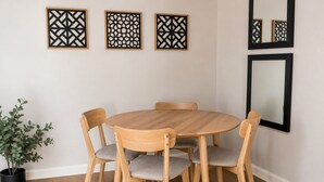 Et spiseområde med et rundt træbord, seks træstole og tre dekorative paneler på væggen.