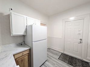 A kitchen with a white refrigerator, wooden cabinets, a marble countertop, and a door with a security lock.