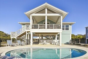 Ein zweistöckiges Haus mit Balkon, Pool und Gartenmöbeln.