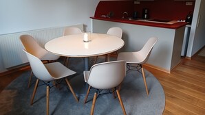 Een eetruimte met een ronde tafel, vier stoelen, een kaars, een hanglamp en een keukenwerkblad met inbouwapparatuur.