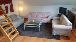 Een woonkamer met een glazen salontafel, gestreepte banken, een houten ladder en een televisie.