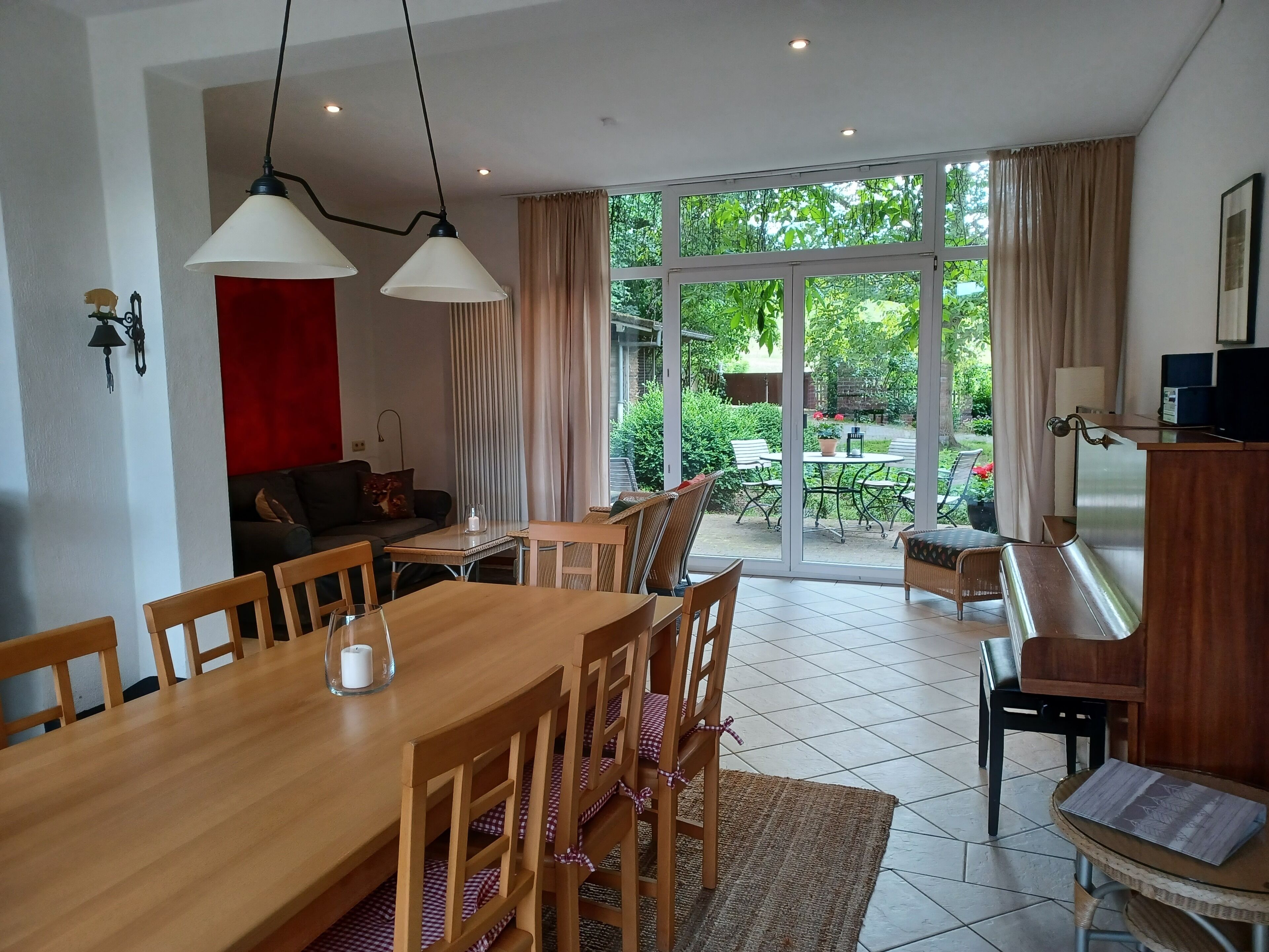 A dining area with a wooden table and chairs, a sofa, and a view of the garden through large windows.