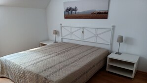 Een slaapkamer met een bed, twee nachtkastjes, een lamp en een schilderij aan de muur.