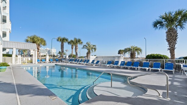 A swimming pool with blue chairs and palm trees. - Grand Caribbean 425 by Liquid Life (Orange Beach)