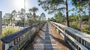 A wooden boardwalk with railings, surrounded by trees and vegetation. - Grand Caribbean 425 by Liquid Life (Orange Beach)