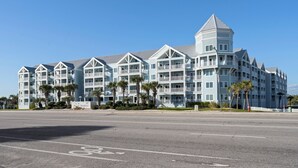 A multi-story hotel with balconies, a central tower, and a parking lot with a bike lane. - Grand Caribbean 425 by Liquid Life (Orange Beach)
