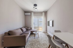 Una sala moderna con sofá, una mesita redonda, una mesa de comedor y un televisor montado en la pared.