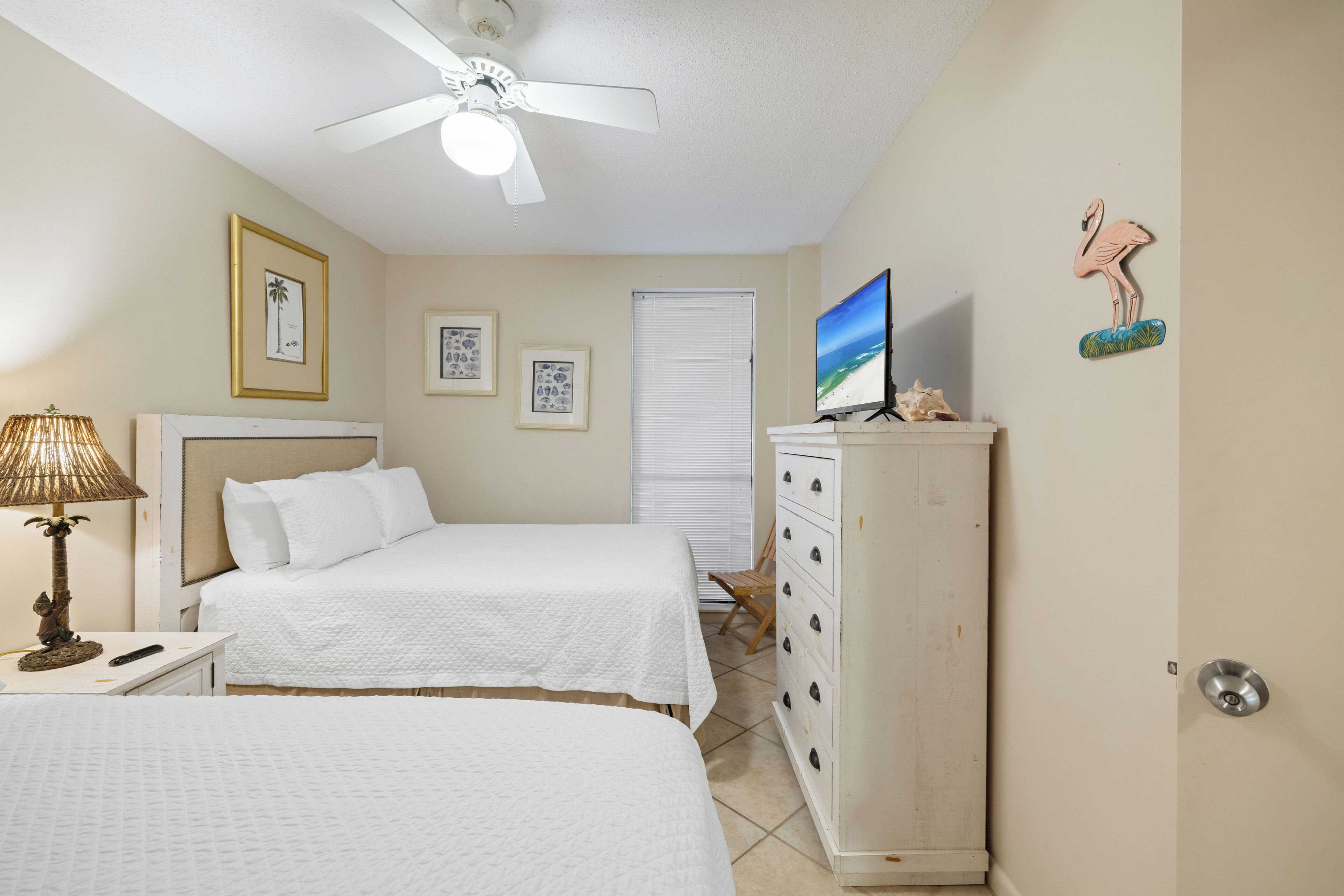 Camera d'albergo con due letti, una ventola a soffitto, televisione, un comò e decorazioni alle pareti.