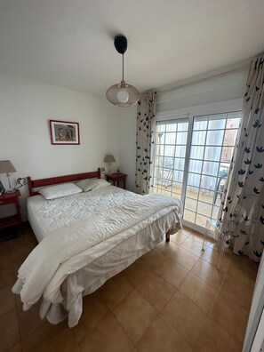 Quarto com cama grande, mesa de cabeceira, abajur, quadro na parede e janela com cortinas.