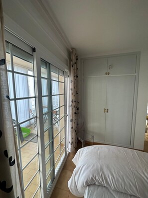 A room with a bed, a wardrobe, and a sliding glass door leading to an outdoor area with a table and chairs. - Maravilloso apartamento al lado de la playa en santa margarita. (Roses)