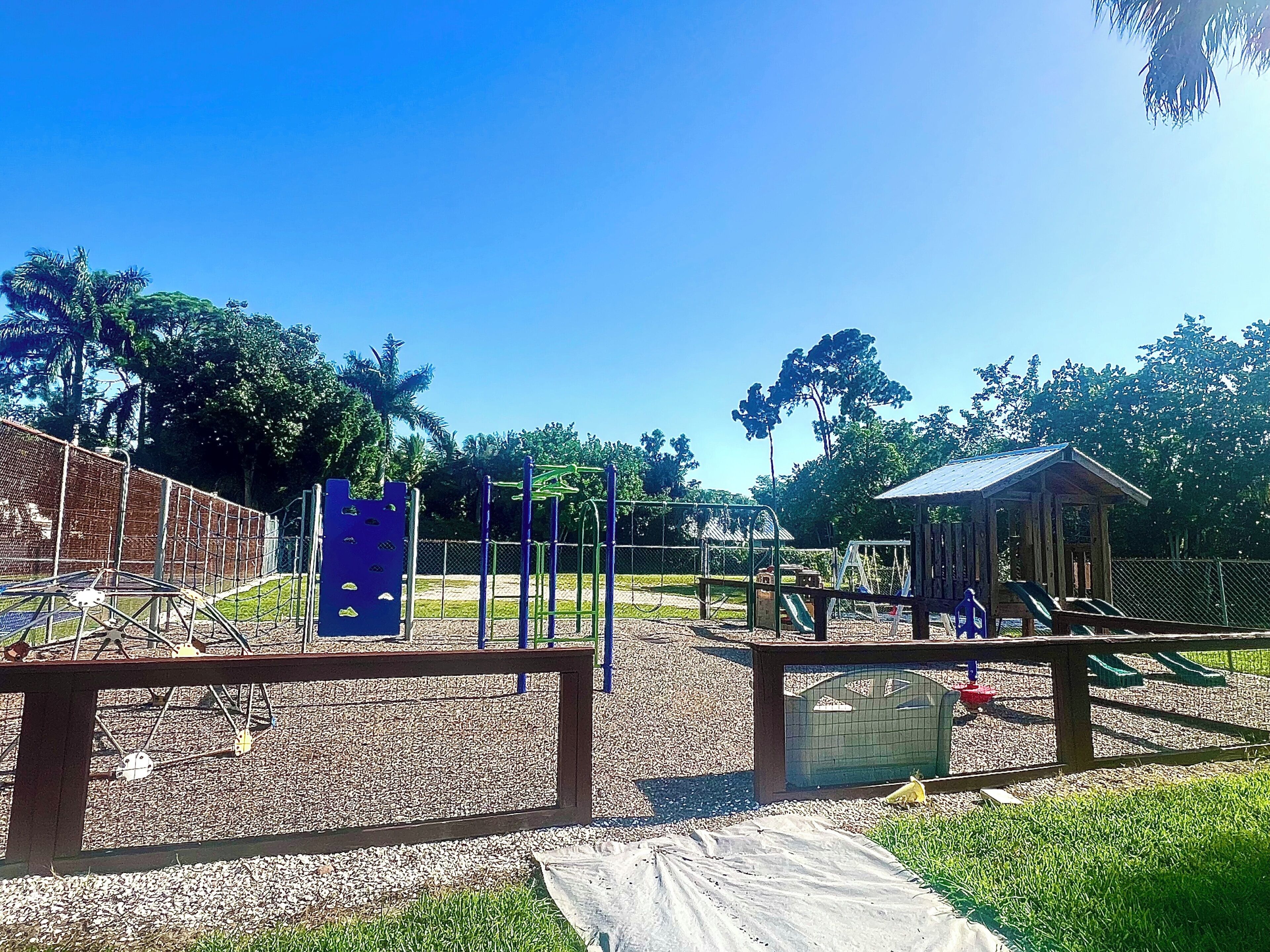 A playground with various play structures, a covered seating area, and a fenced play area.